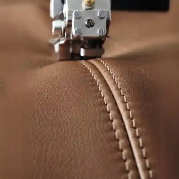 How to Cover a Leather Sofa with Fabric showing a close-up of a sewing machine stitching brown leather upholstery with precision for a fabric overlay