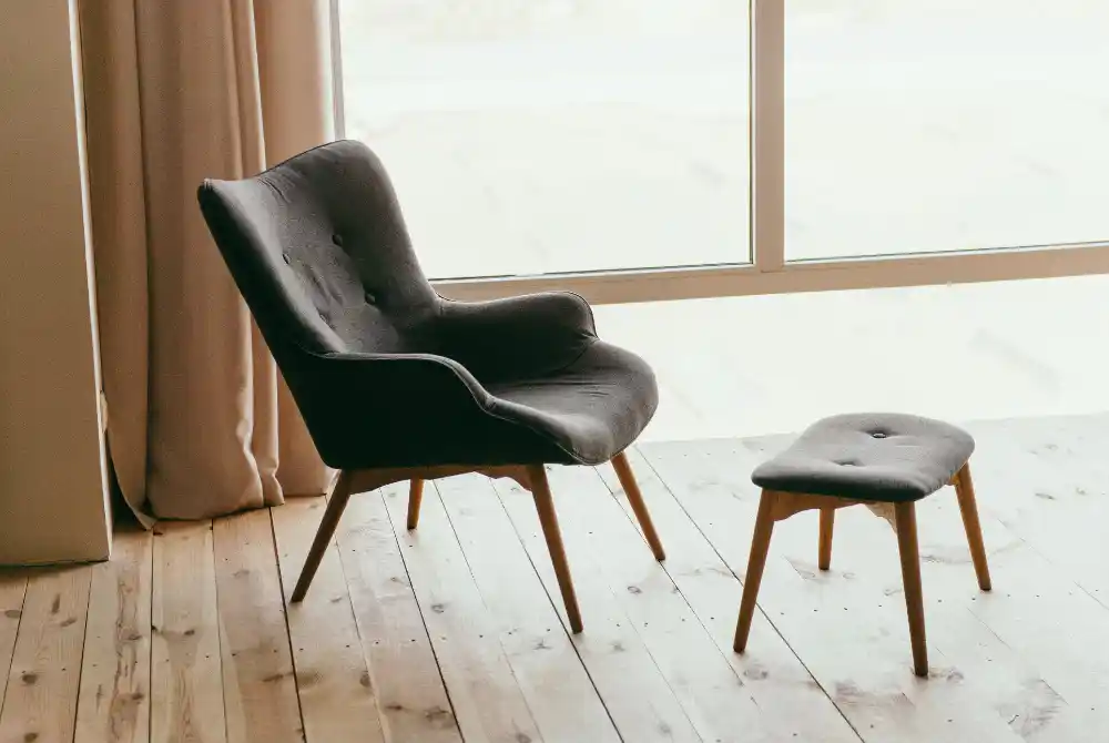 Modern wooden chair with beige sofa upholstery and a white cushion placed against a wooden wall.