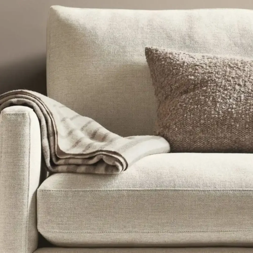 How to wash linen sofa covers showing a soft beige linen sofa with a textured cushion and folded throw blanket in a clean, cozy living room setting